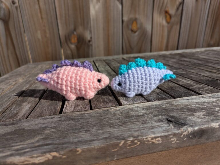 Two crocheted dinosaur minis on a wooden table