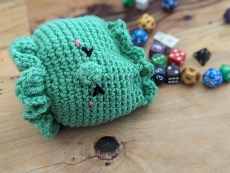 A green crocheted octopus dice bag beside a pile of dice
